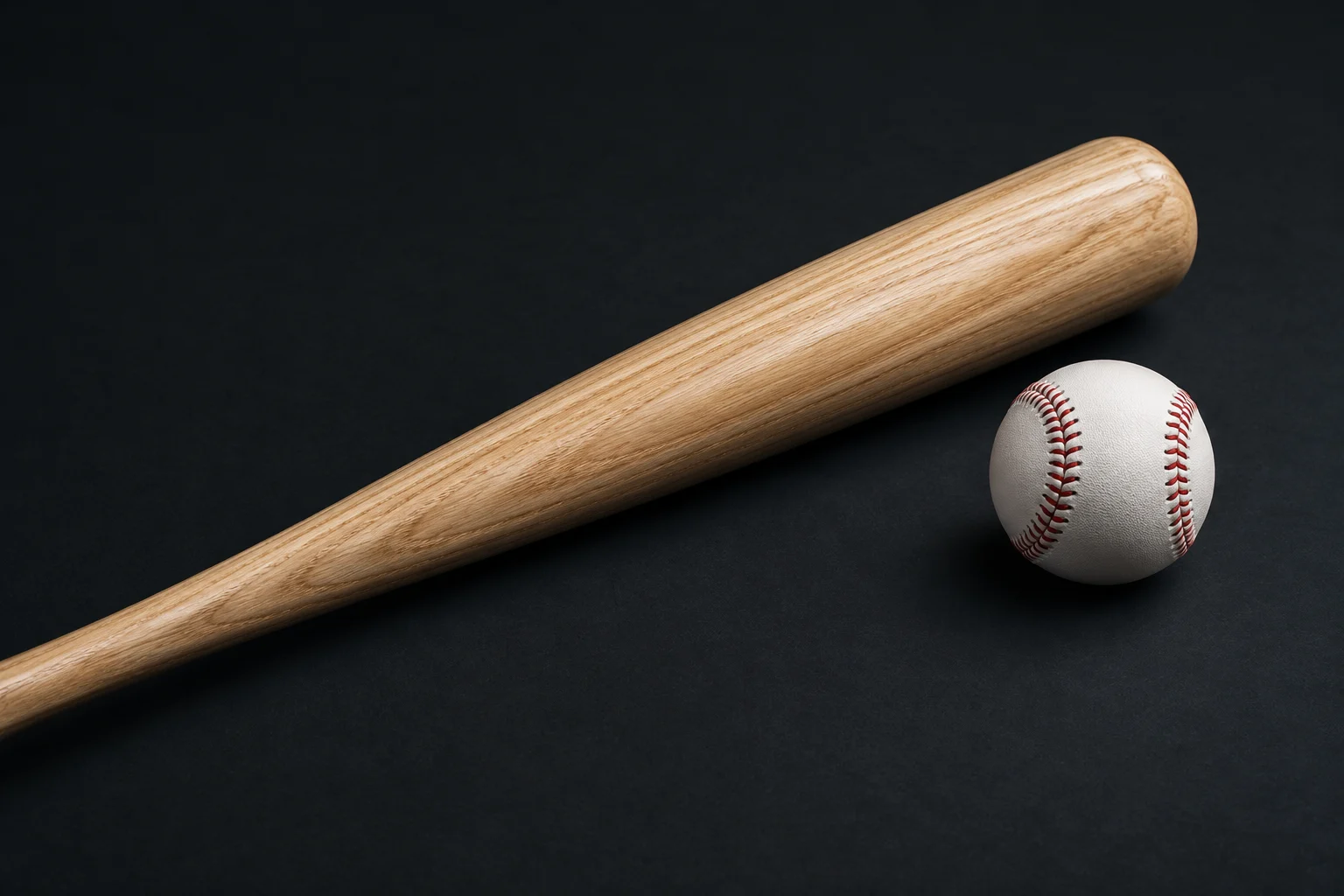 A wood bat and baseball on a dark surface.